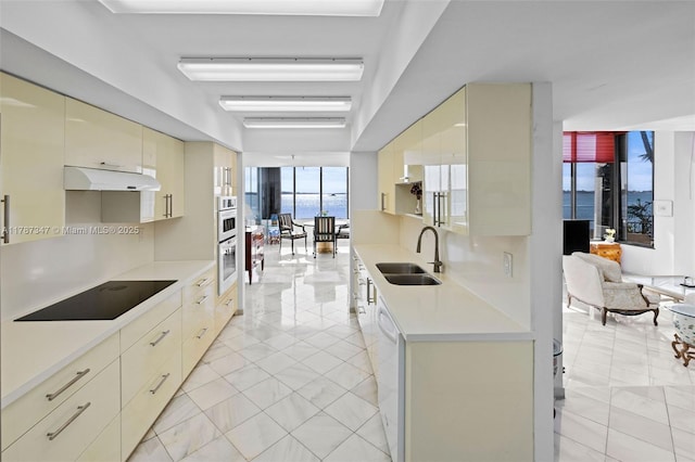 520 Brickell Key Dr Unit A201, Miami, FL 33131 - kitchen with cream cabinetry, under cabinet range hood, light countertops, a sink, and black electric stovetop