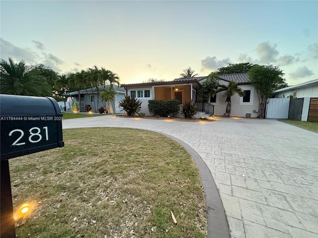 ranch-style house with a yard, a tiled roof, stucco siding, curved driveway, and fence