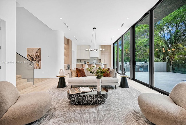 living room with recessed lighting, stairway, light wood finished floors, a wall of windows, and a notable chandelier