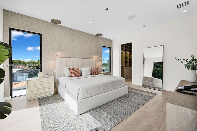 bedroom with access to exterior, baseboards, visible vents, a spacious closet, and wood finished floors