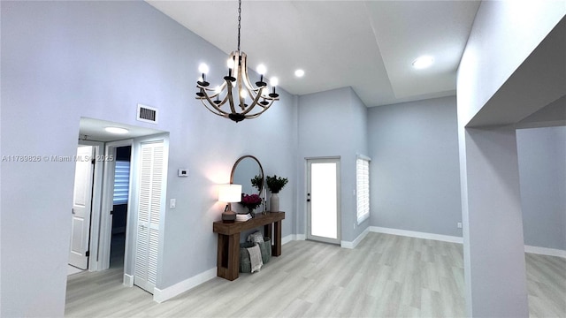 foyer entrance featuring visible vents, an inviting chandelier, baseboards, wood finished floors, and a high ceiling