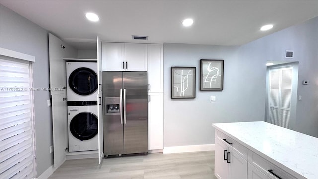 kitchen with stainless steel fridge with ice dispenser, stacked washer / drying machine, light wood-style flooring, baseboards, and white cabinetry
