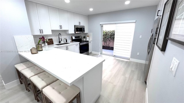 12239 NW 7th St, Miami, FL 33182 - kitchen with stainless steel appliances, a sink, a breakfast bar area, light wood-style flooring, and baseboards
