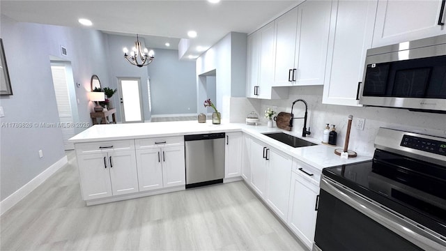 kitchen featuring a sink, stainless steel appliances, white cabinets, a peninsula, and a notable chandelier