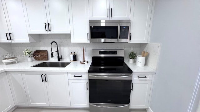 kitchen with white cabinets, stainless steel appliances, a sink, tasteful backsplash, and light stone counters