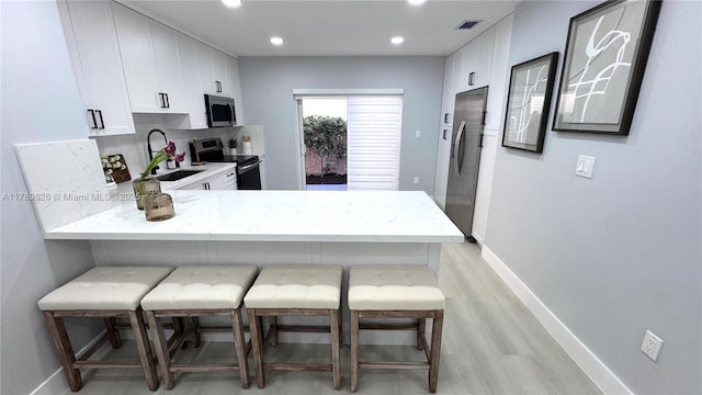 kitchen featuring visible vents, a sink, baseboards, a peninsula, and appliances with stainless steel finishes