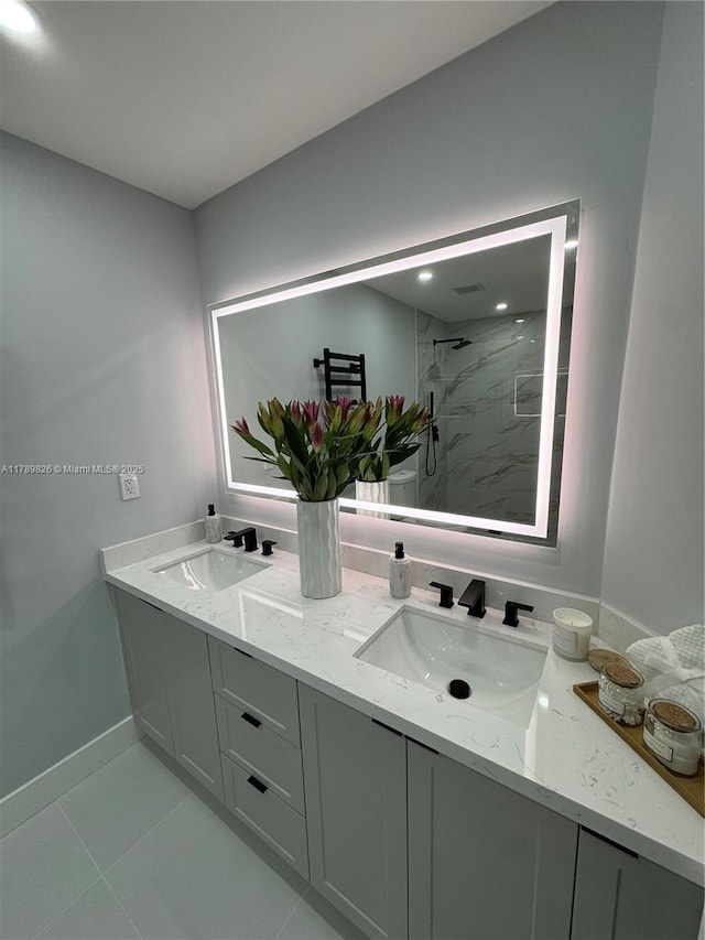 bathroom with a tile shower, baseboards, a sink, and double vanity