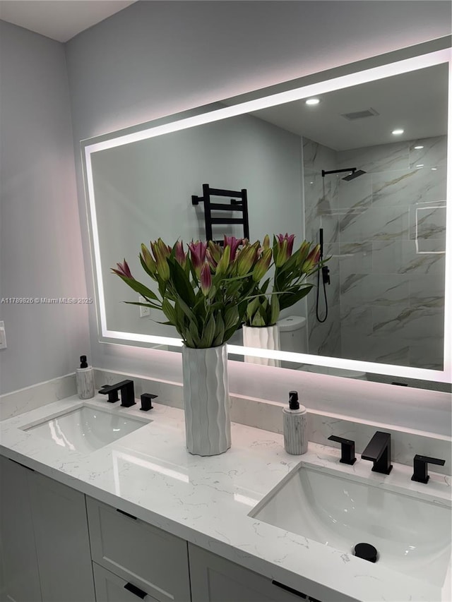 bathroom with toilet, a marble finish shower, a sink, and double vanity