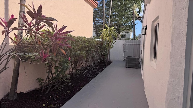 view of side of home featuring stucco siding, central AC unit, and fence