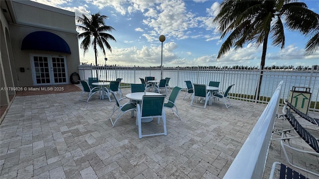 view of patio / terrace with fence, french doors, outdoor dining space, and a water view