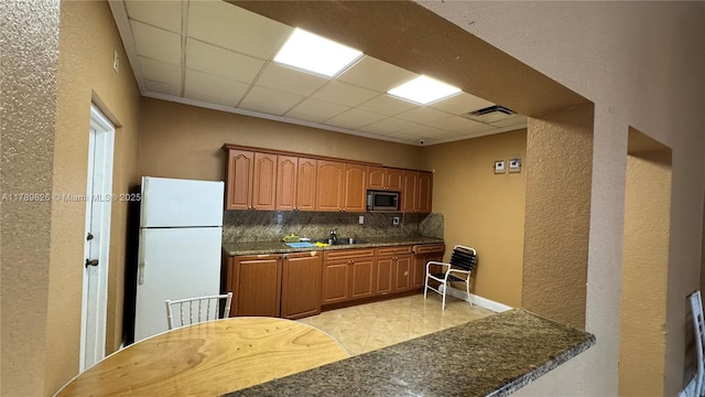 kitchen featuring stainless steel microwave, a sink, a drop ceiling, and freestanding refrigerator