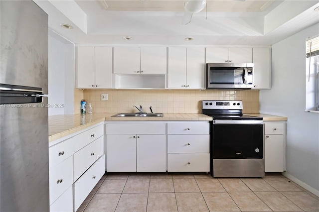 kitchen featuring appliances with stainless steel finishes, tile counters, a raised ceiling, and a sink
