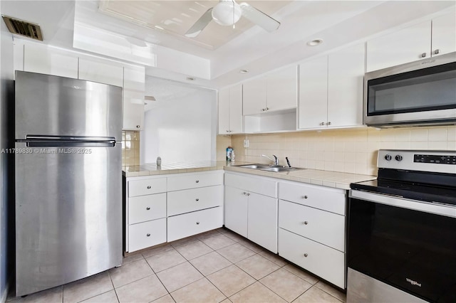 kitchen with white cabinetry, tasteful backsplash, a sink, appliances with stainless steel finishes, and tile counters