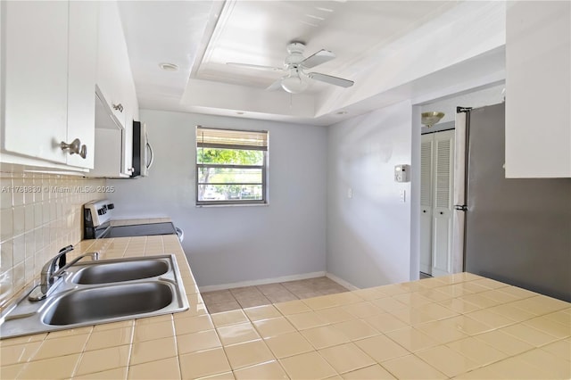 kitchen with decorative backsplash, tile counters, appliances with stainless steel finishes, a sink, and a ceiling fan