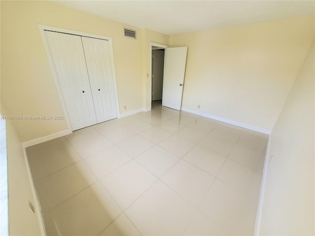 unfurnished bedroom featuring light tile patterned floors, baseboards, visible vents, and a closet