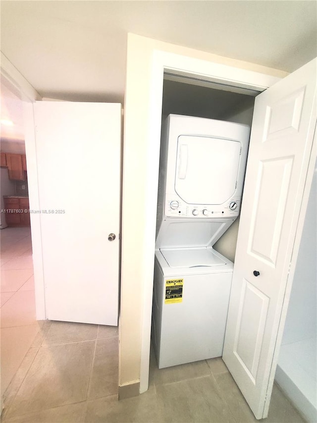 clothes washing area featuring light tile patterned flooring, stacked washer / drying machine, and laundry area