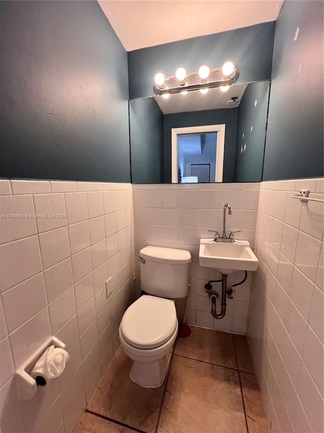half bathroom with toilet, tile walls, a sink, and tile patterned floors