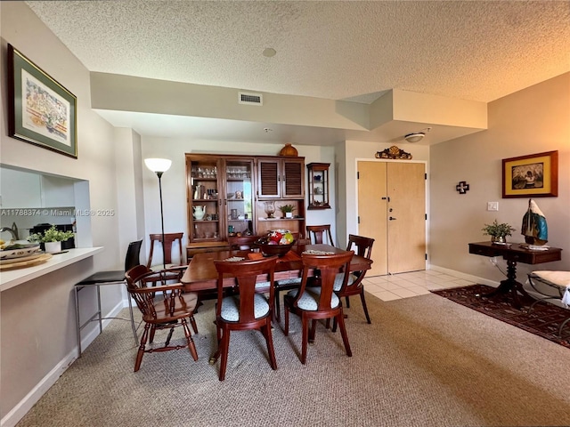 dining area with light colored carpet, baseboards, a textured ceiling, and visible vents