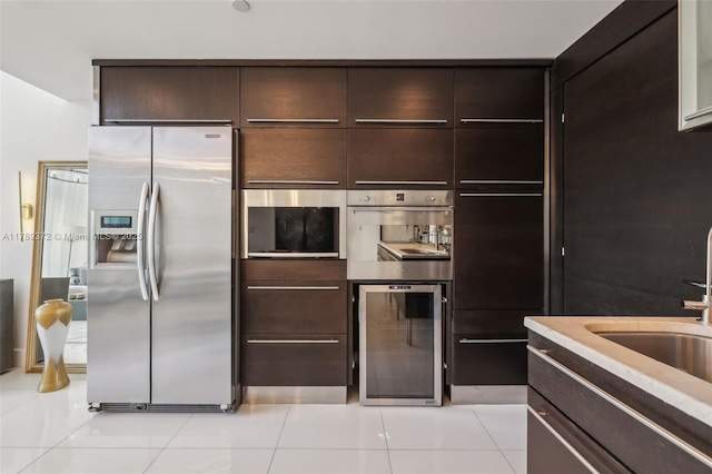 kitchen featuring wine cooler, dark brown cabinets, light tile patterned floors, a sink, and appliances with stainless steel finishes