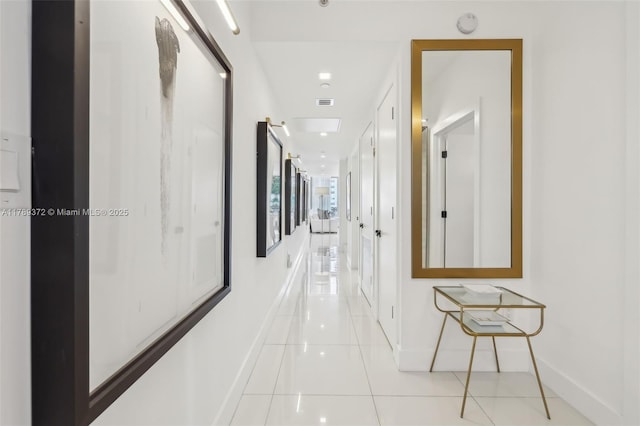 corridor with baseboards, visible vents, and light tile patterned floors
