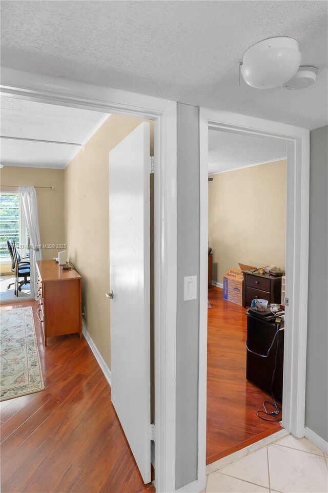 hallway with baseboards, wood finished floors, and a textured ceiling