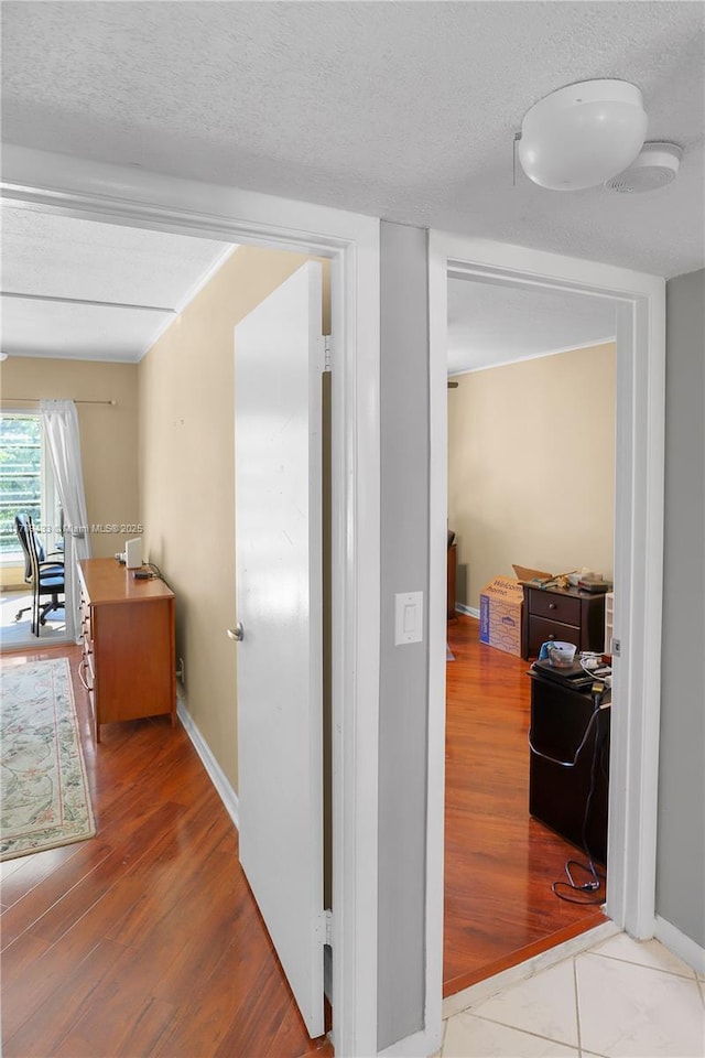 hall with baseboards, wood finished floors, and a textured ceiling