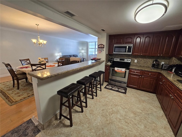 5825 Collins Ave Unit 2D, Miami Beach, FL 33140 - kitchen featuring tasteful backsplash, a breakfast bar, visible vents, stainless steel appliances, and ornamental molding