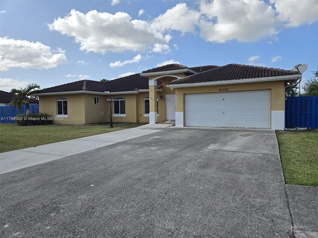 prairie-style house with driveway, fence, a front yard, a garage, and stucco siding