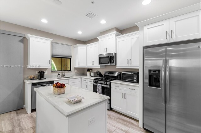 kitchen with a sink, stainless steel appliances, white cabinetry, visible vents, and a kitchen island