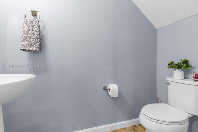 half bathroom featuring toilet, wood finished floors, vaulted ceiling, and baseboards