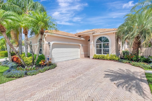 mediterranean / spanish-style home featuring a tile roof, decorative driveway, stucco siding, and a garage
