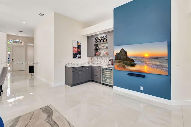 bar with beverage cooler, decorative backsplash, bar, baseboards, and visible vents