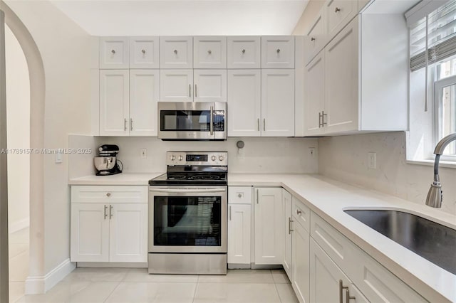 kitchen with a sink, light tile patterned flooring, light countertops, arched walkways, and appliances with stainless steel finishes