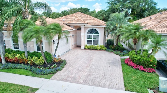 mediterranean / spanish home with stucco siding, a tile roof, decorative driveway, and an attached garage