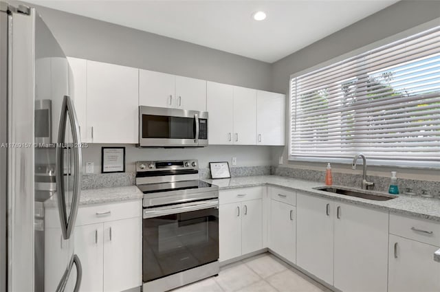 kitchen with light tile patterned floors, white cabinetry, a sink, stainless steel appliances, and light stone countertops