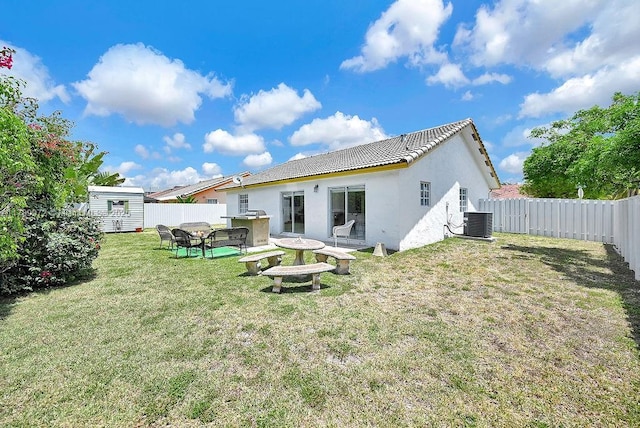 rear view of property with an outdoor structure, a shed, stucco siding, central AC, and a fenced backyard