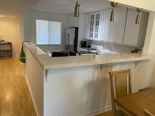 kitchen featuring glass insert cabinets, light wood finished floors, a kitchen bar, a peninsula, and freestanding refrigerator