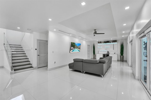 living area with light tile patterned flooring, a ceiling fan, stairway, and a raised ceiling
