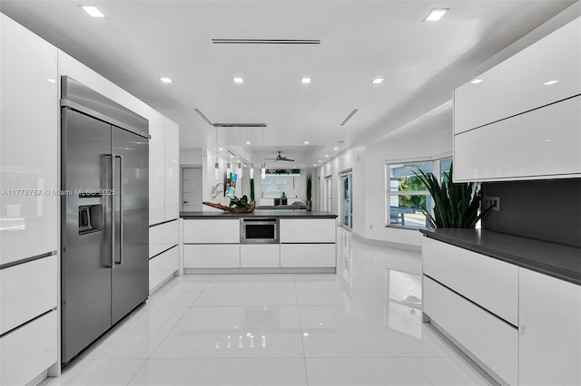 kitchen with dark countertops, built in refrigerator, modern cabinets, and white cabinetry