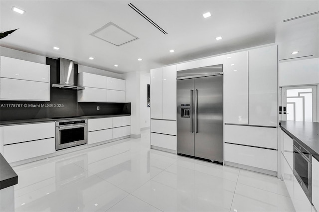 kitchen with wall chimney exhaust hood, built in appliances, modern cabinets, and dark countertops