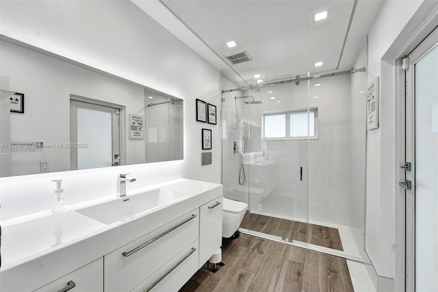 bathroom with visible vents, vanity, wood finished floors, toilet, and a shower stall