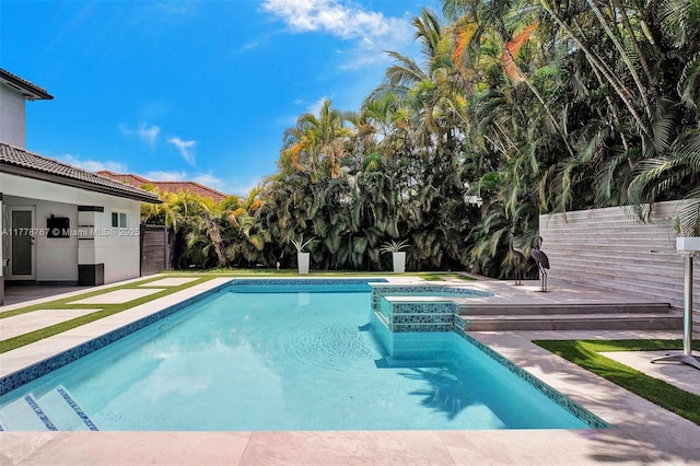 view of pool with fence and a pool with connected hot tub