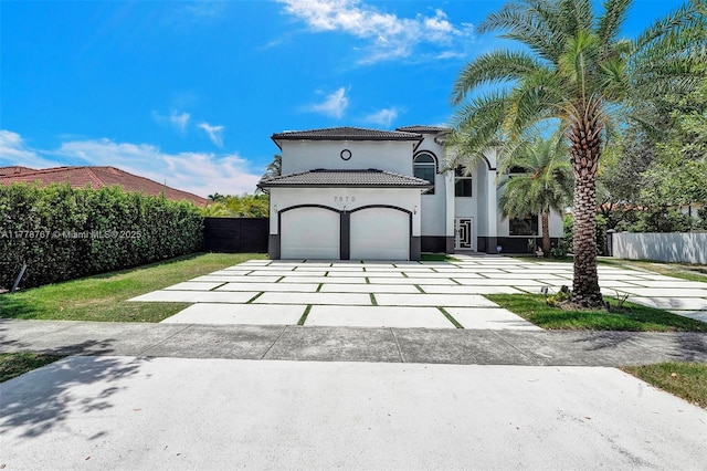 mediterranean / spanish house with fence, stucco siding, a tiled roof, an attached garage, and driveway