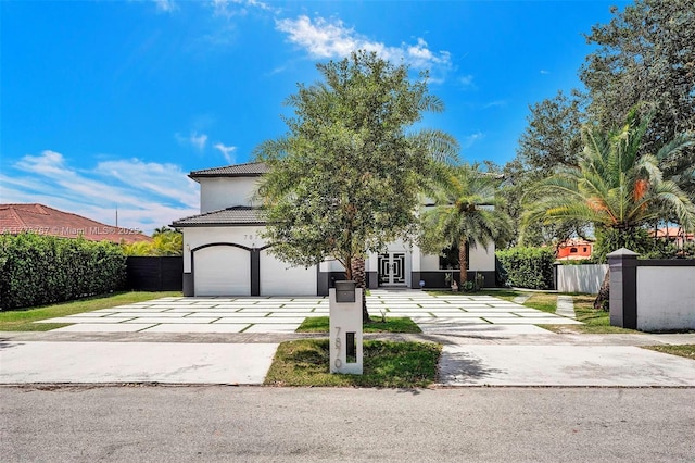 view of property hidden behind natural elements with driveway, french doors, a tile roof, a garage, and fence