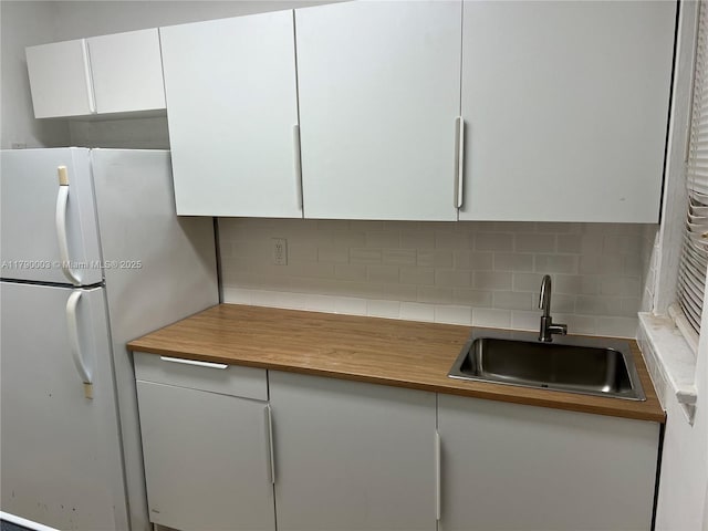 kitchen featuring white cabinets, freestanding refrigerator, a sink, and tasteful backsplash