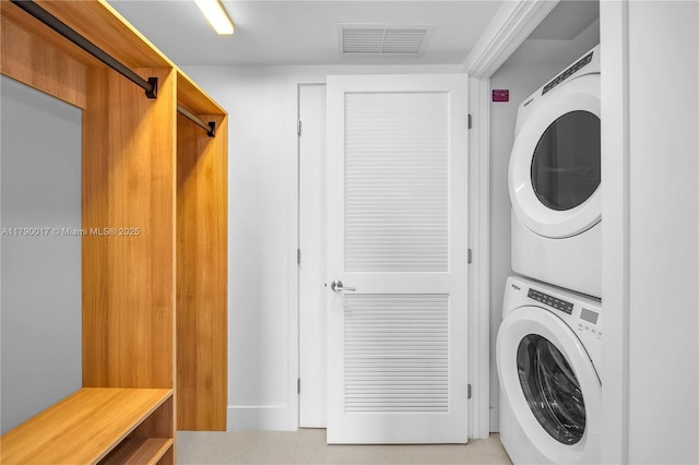 clothes washing area featuring stacked washer and clothes dryer, visible vents, and laundry area