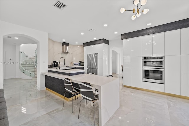 kitchen with visible vents, modern cabinets, arched walkways, wall chimney exhaust hood, and appliances with stainless steel finishes