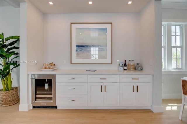 bar featuring beverage cooler, a dry bar, light wood-style flooring, and baseboards
