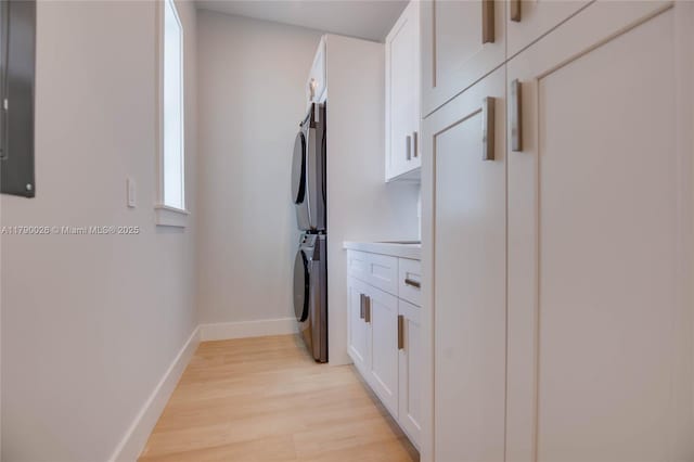 clothes washing area featuring cabinet space, stacked washer / drying machine, baseboards, and light wood-style flooring