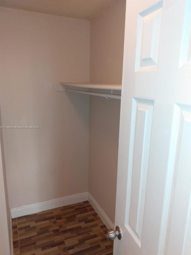 walk in closet with dark wood-style floors